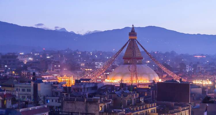 Vue du soir d'un grand stupa illuminé, avec les lumières de la ville en arrière-plan.