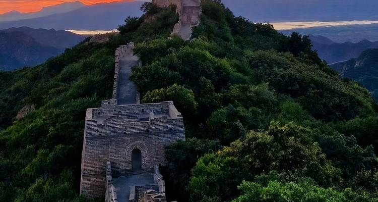 Sunset view of the Great Wall of China winding over a green mountain.