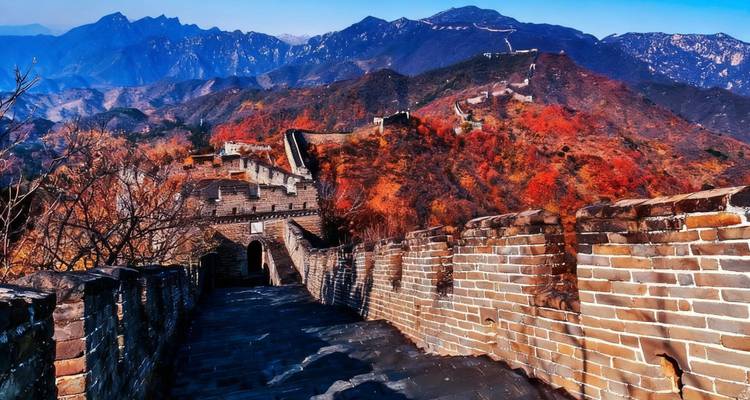 The Great Wall of China on a mountain ridge with autumn colors surrounding it.