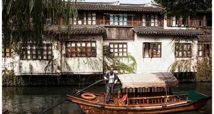 Man steering a traditional wooden boat on a peaceful canal.
