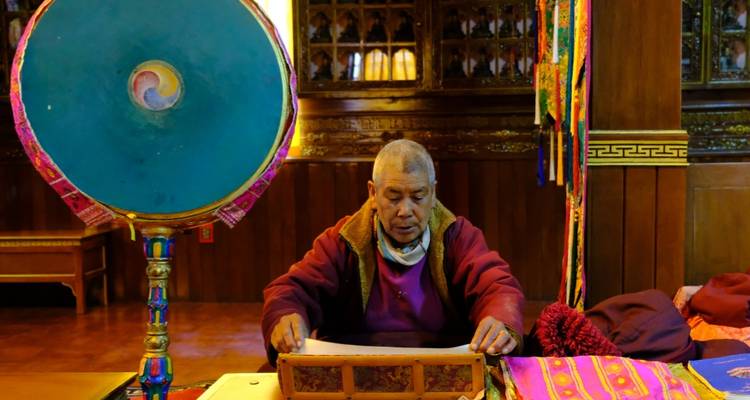 Monk sitting at a table with colorful religious objects inside a temple.