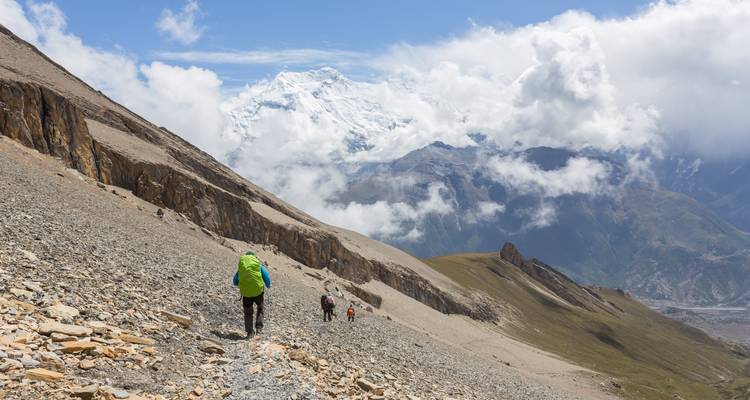 Randonneurs marchant sur un sentier rocheux avec des montagnes enneigées.