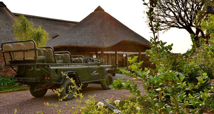 Exterior of a lodge with a safari vehicle parked nearby.