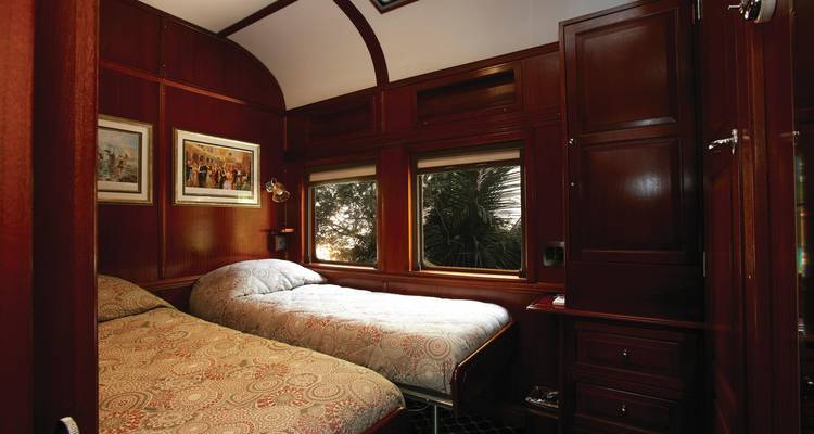 Train cabin with twin beds and windows showing landscape.