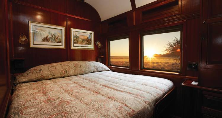 Train cabin with a large bed and views of a sunset.