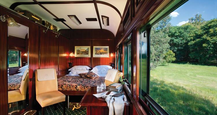 Train cabin with a bed, large windows, and scenic view.