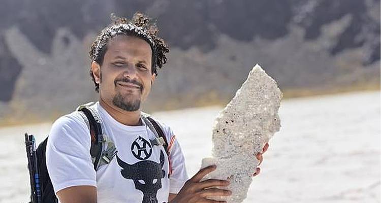 Personne tenant un gros fragment de roche dans un paysage rocheux.