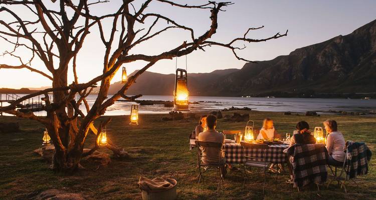 A group dining alfresco by candlelight with a mountain backdrop.