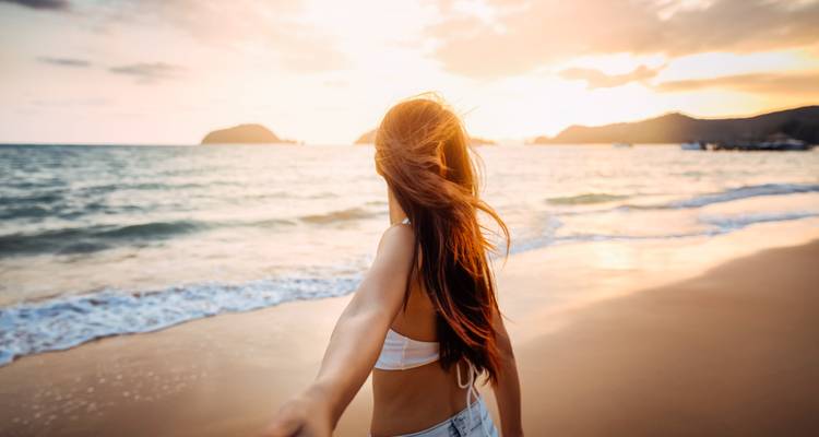 Femme debout sur une plage au coucher du soleil avec une vue sur l'océan.