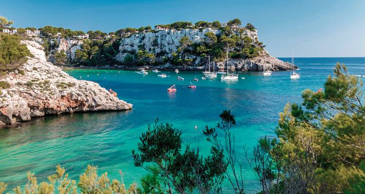 Beautiful turquoise bay with boats and cliffside greenery.
