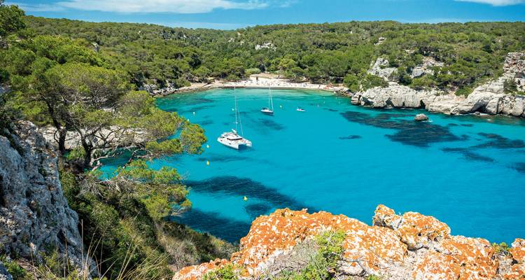 Vibrant blue bay with anchored boats surrounded by lush green cliffs.