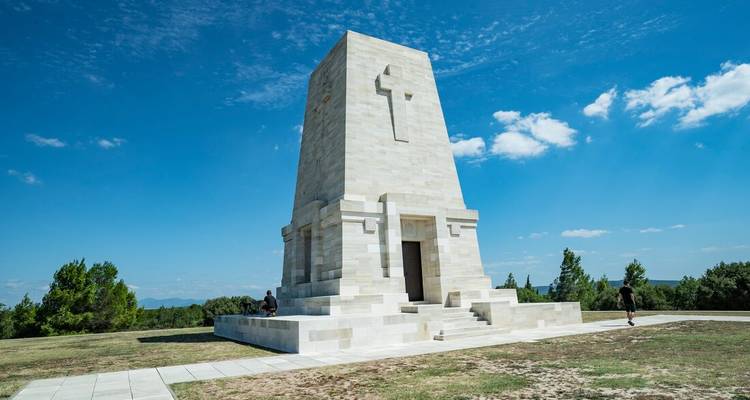 People sitting near a white stone monument with a cross.