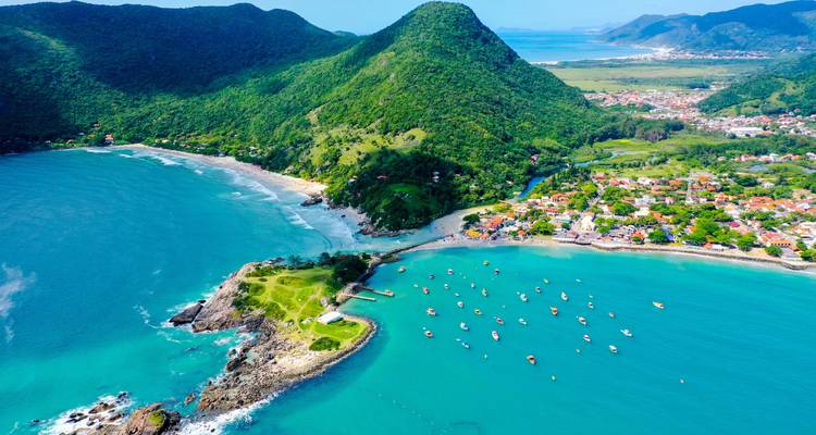 Aerial view of a coastal area with hills, beaches, and boats in turquoise waters.