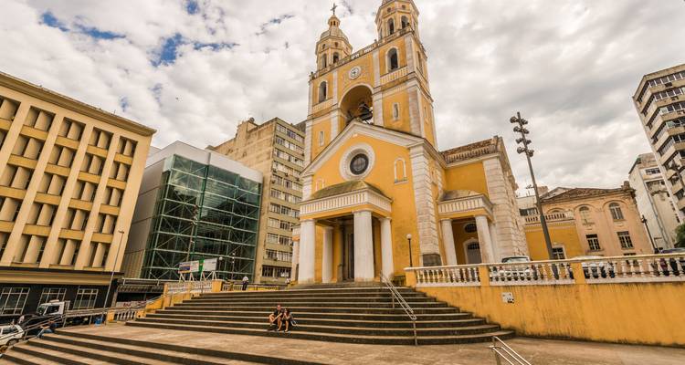 A large yellow church with two towers and people sitting on the stairs in front.