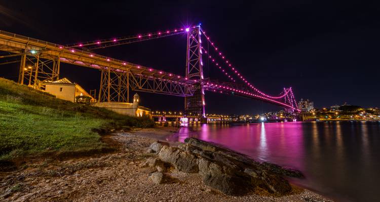 A brightly lit bridge at night with reflections on the water.
