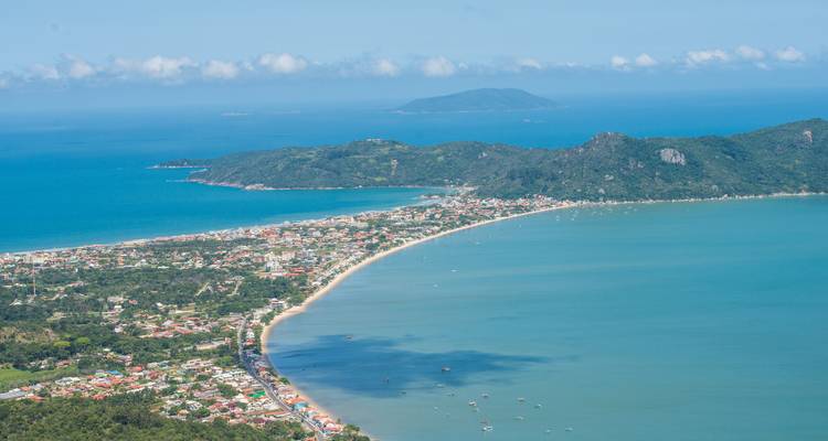 Aerial view of a coastline with a long beach and surrounding hills.