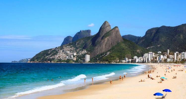 A sandy beach with people and mountains in the background.