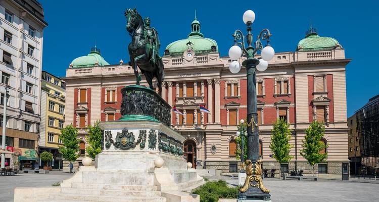 Statue in front of a grand building with green domes.