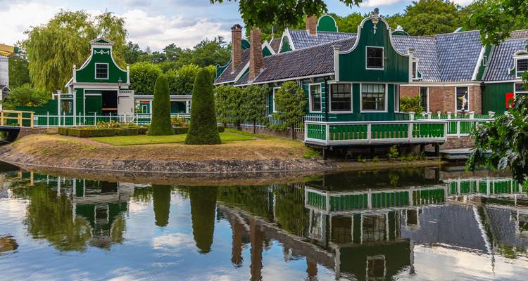 Maisons traditionnelles en bois vert foncé avec des garnitures blanches se reflétant dans un canal immobile bordé d'arbres.