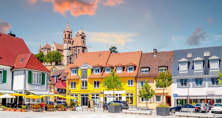 Plaza de pueblo encantadora con edificios coloridos y una iglesia al fondo.