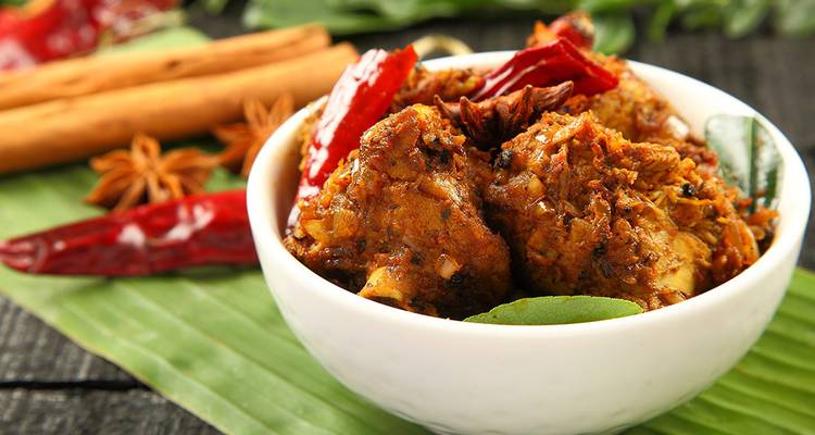 Un bol de curry de poulet épicé garni d'épices sur une feuille de bananier.