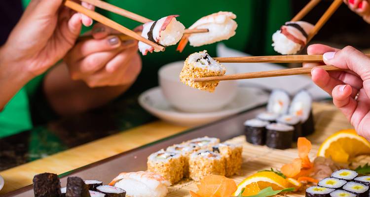 People enjoying sushi with chopsticks around a table.