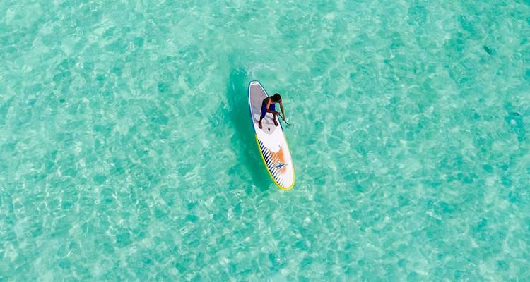 Person paddleboarding on clear turquoise water.