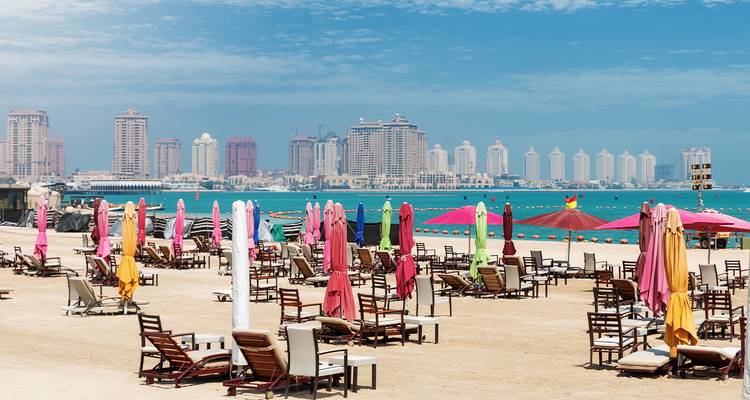 Kleurrijk strand met parasols en stadshorizon op de achtergrond.