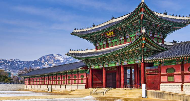 Traditional Korean palace with mountain backdrop under blue sky.