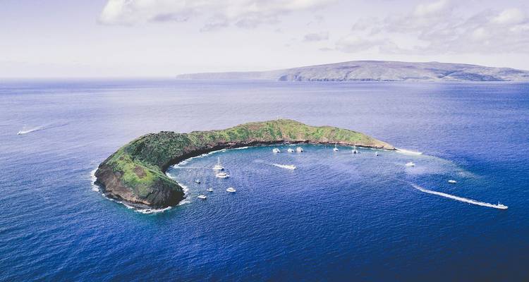 Vue aérienne de l'îlot en forme de croissant de Molokini entouré de bateaux de visite touristique sur les eaux bleu profond de l'océan Pacifique au large de Maui.