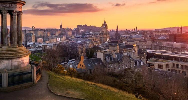 Panorama del atardecer de Edimburgo desde Calton Hill con luz cálida sobre los techos de piedra históricos y el horizonte.