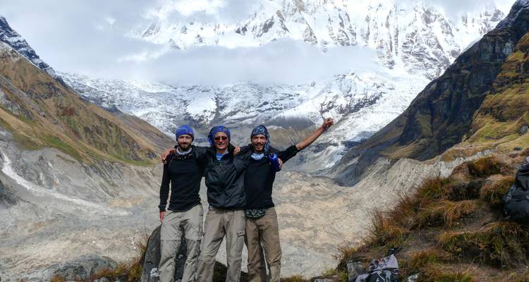 Drei Wanderer posieren triumphierend mit schneebedeckten Bergen im Hintergrund.