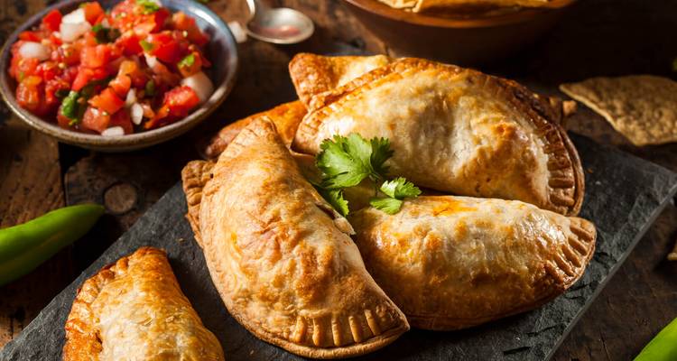 Traditionelle argentinische Empanadas mit Salsa serviert auf einer Schieferplatte.