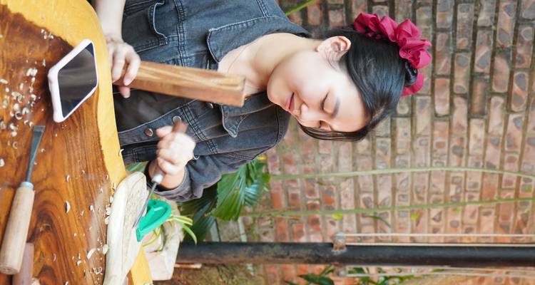Young woman crafting with tools on a table, surrounded by plants.