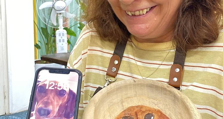 Smiling woman holding a carved wooden object and a phone.