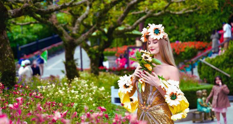 Vrouw in bloemrijke kleding omringd door bloemen in een tuin.