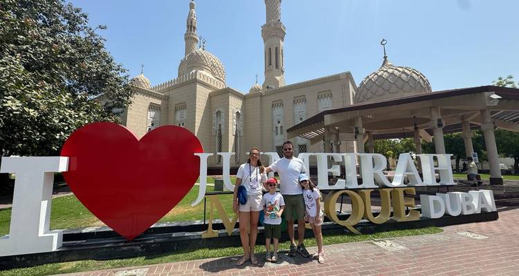 Famille posant devant une mosquée avec un panneau touristique.