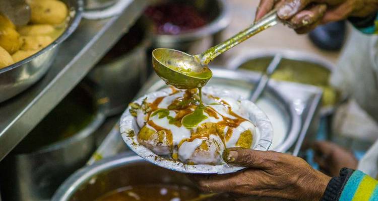 Personne préparant de la cuisine de rue indienne avec diverses garnitures.
