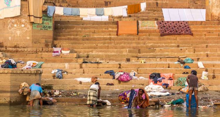 Des gens lavant des vêtements le long des marches de la rivière avec du linge coloré.