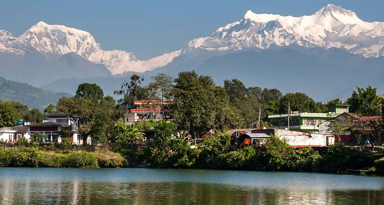 Ville pittoresque au bord d'un lac avec des montagnes enneigées en arrière-plan.