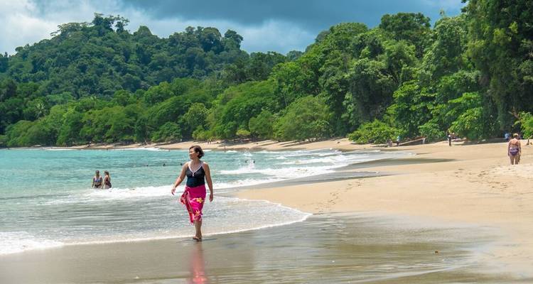 Woman walking on a sandy beach with ocean waves.