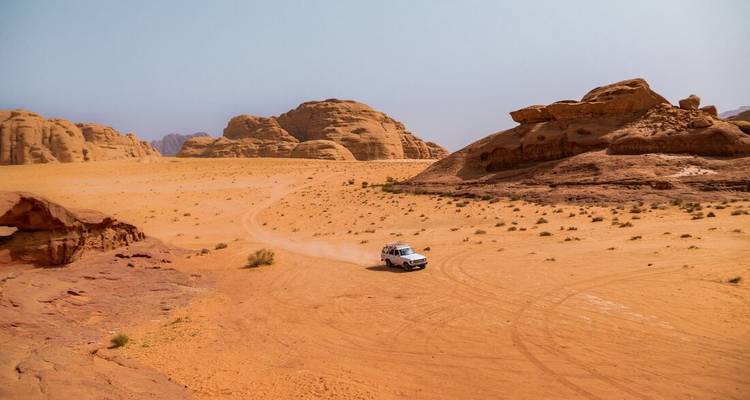 Paysage désertique avec un véhicule roulant sur des pistes sableuses.
