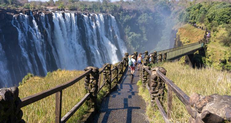 View of Victoria Falls with a pathway leading to the edge and people walking.