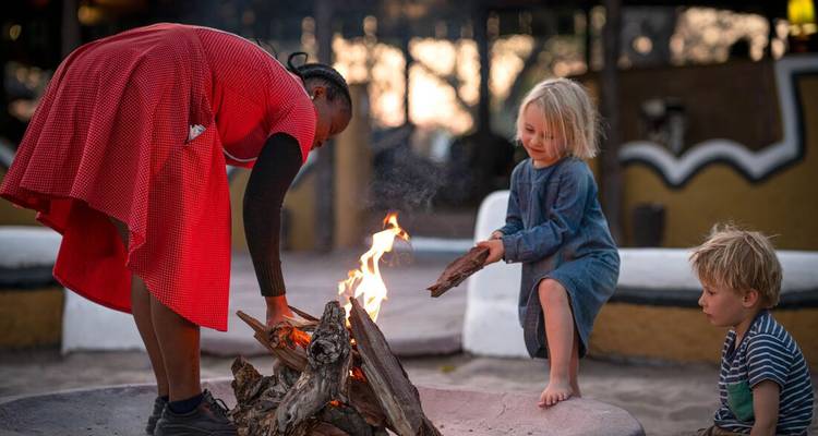 Children and a woman sitting around a campfire.