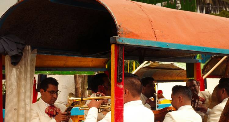 Des musiciens de mariachi en costume blanc accordent leurs instruments à bord d'une barque fluviale aux couleurs vives.