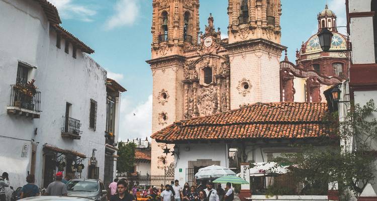 Rue coloniale animée à Taxco avec des foules de personnes et les deux tours ornées de l'église Santa Prisca s'élevant derrière.