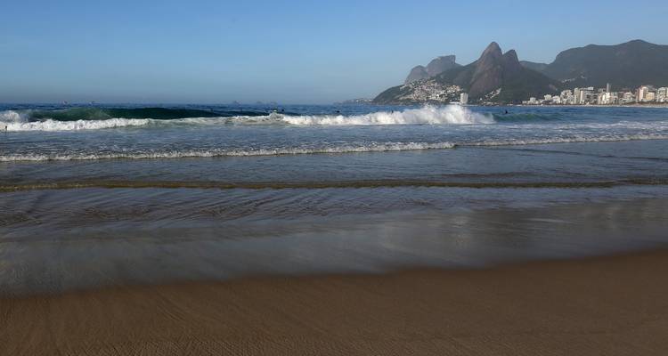 Waves crashing on a beach with mountains in the distance in Rio de Janeiro.