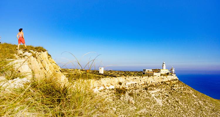 Person enjoying a scenic walk along a cliff with a lighthouse.