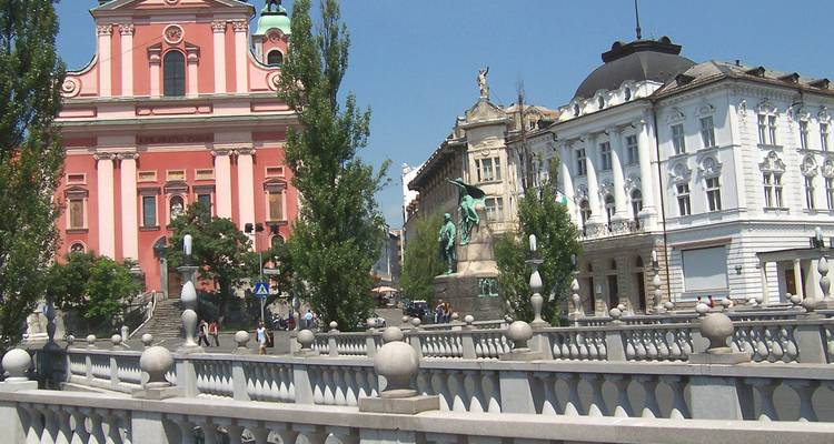Ljubljana Stadtbild mit einer markanten rosa Kirche und Menschen, die über eine Brücke gehen.