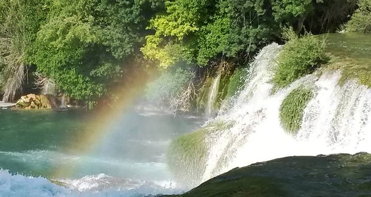 Wasserfall mit sichtbarem Regenbogen und umgeben von Grün im Krka-Nationalpark.